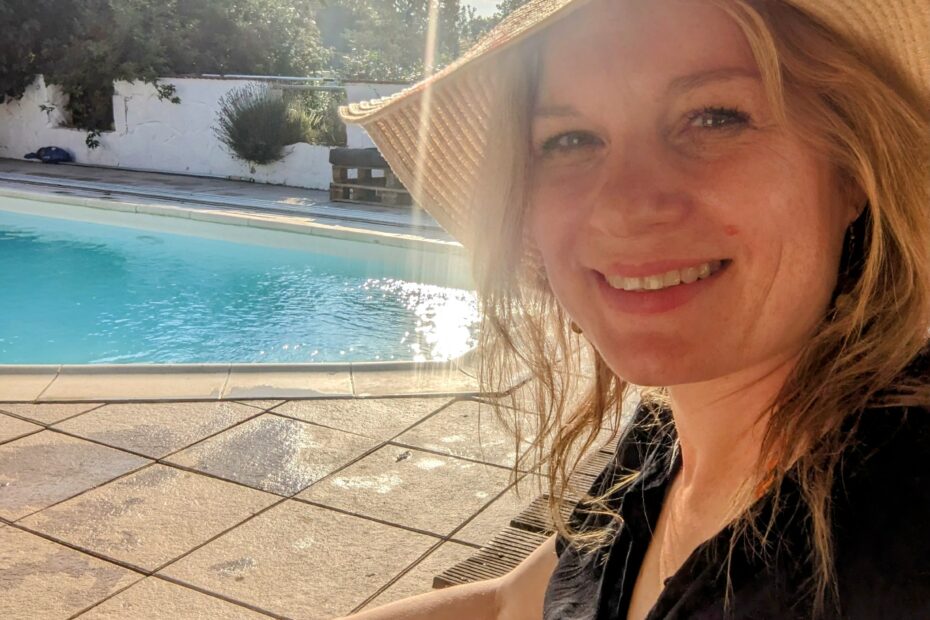 Foto von Ukulili mit Lächeln, schwarzem Kleid und Sonnenhut vor einem Pool