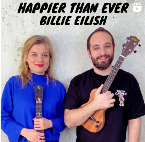 Foto von Ukulili und VIncenzo. Sie trägt blauen Rollkragenpullover und blaue Ukulele., dazu blonde lange Haare und roten Lippenstift. Er trägt ein schwarzes T-Shirt und eine braune Ukulele. Beide lächeln in die Kamera. Überschrift "Happier than ever" - Billie Eilish